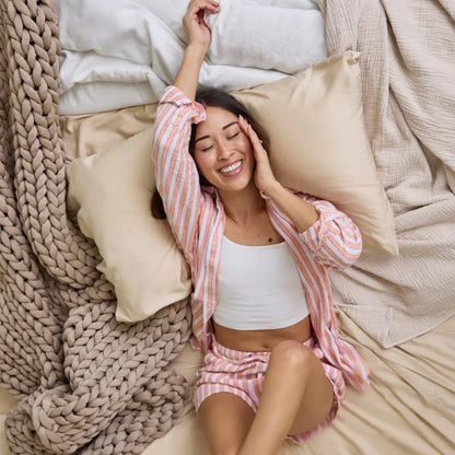 Woman relaxing on bed with chunky knit weighted blanket in beige, cozy bedding