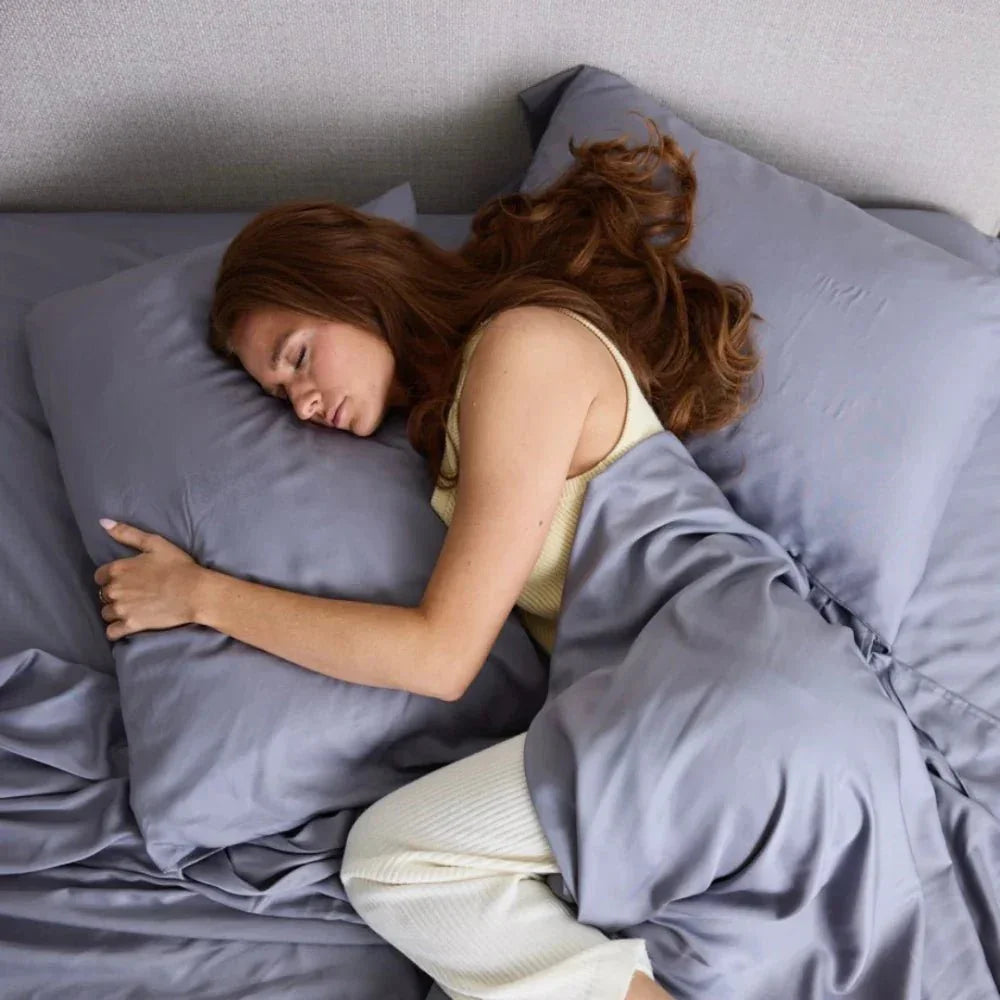 Woman sleeping peacefully with a gray cooling weighted blanket on a bed
