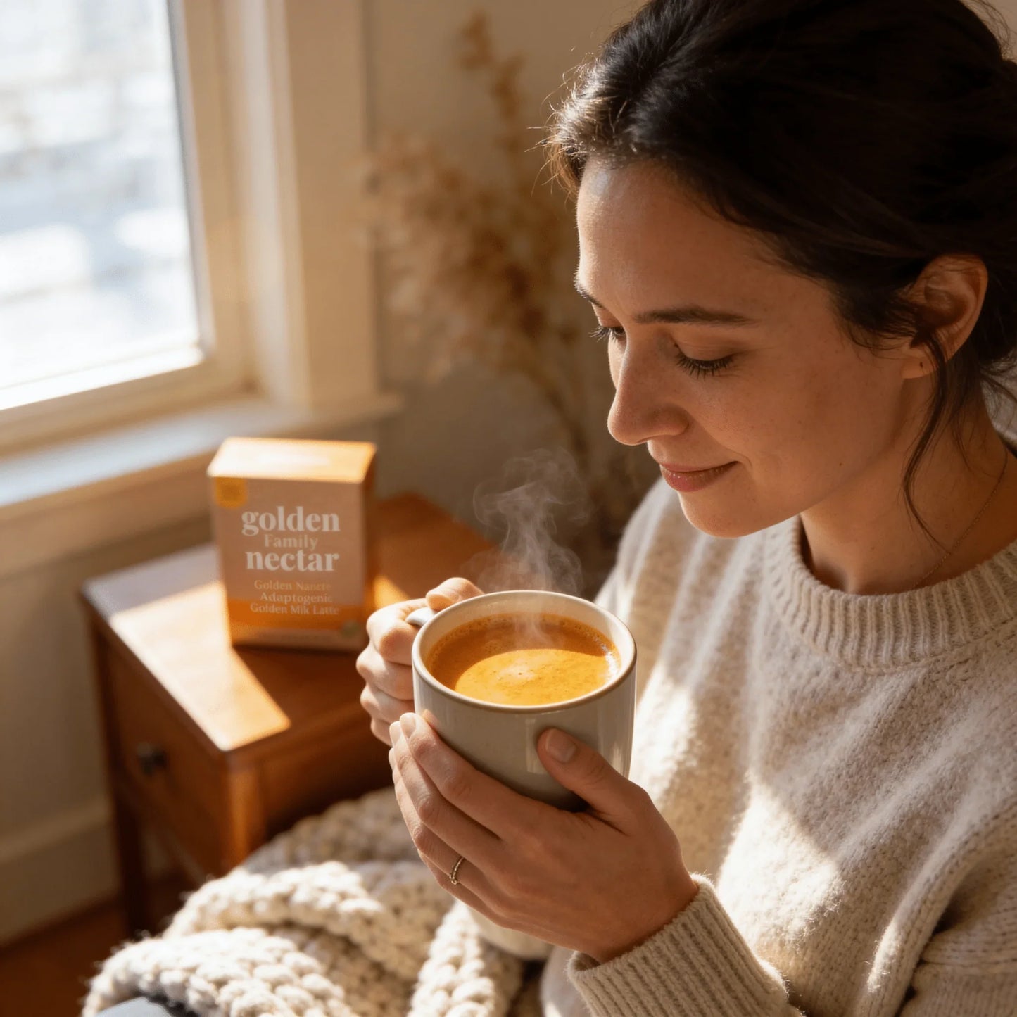 Woman enjoying a warm golden milk latte in a cozy home setting, adaptogenic latte box nearby.