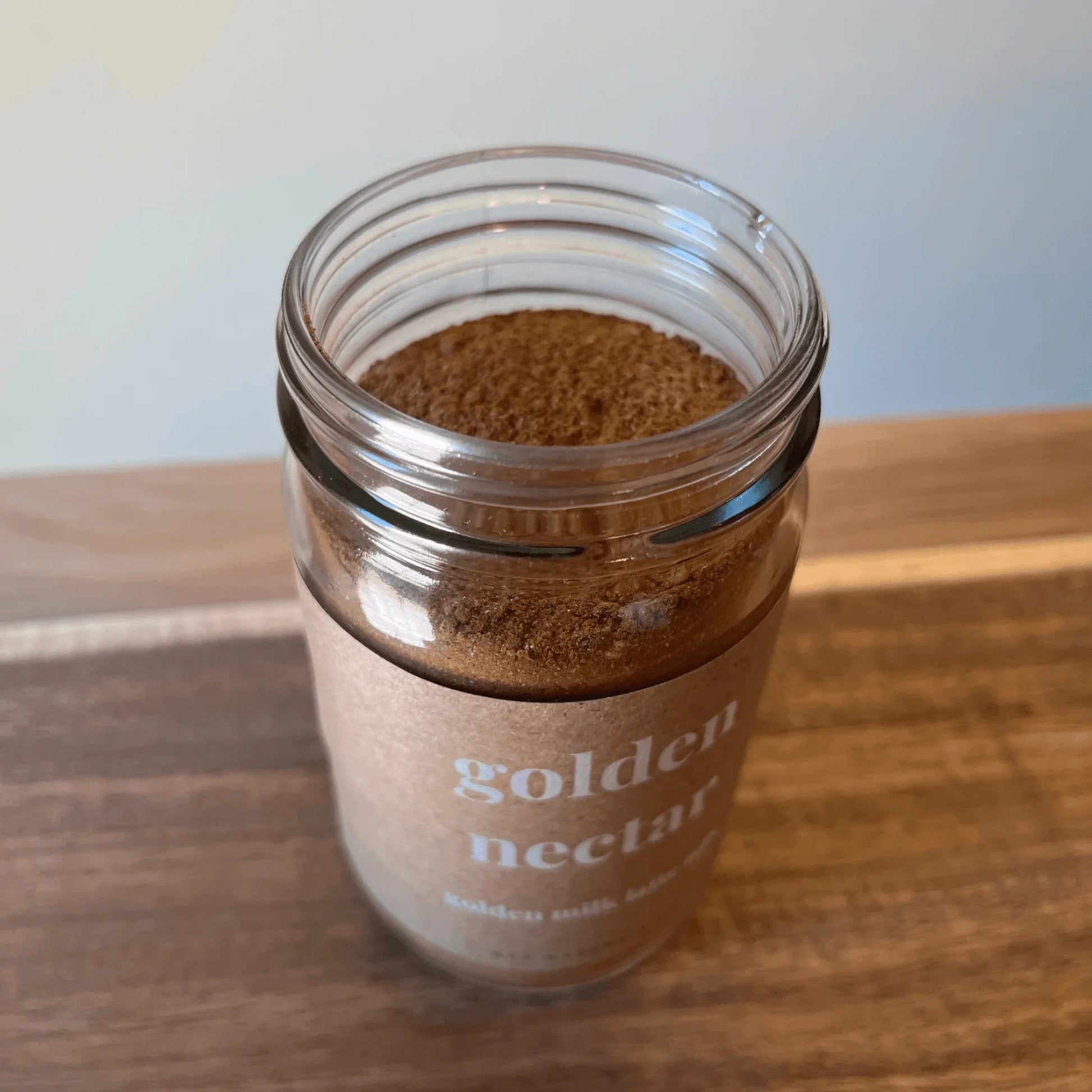 Golden Nectar adaptogenic golden milk latte mix powder in a clear glass jar on a wood surface
