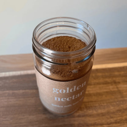 Golden Nectar adaptogenic golden milk latte mix powder in a clear glass jar on a wood surface