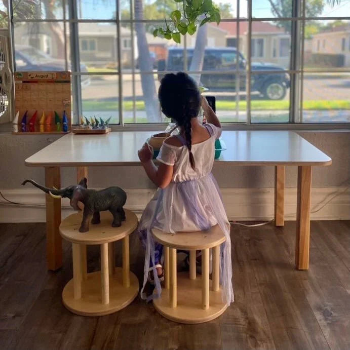Child in sensory-friendly dress sitting at kids' activity table with wooden stools and elephant toy