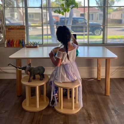 Child in sensory-friendly dress sitting at kids' activity table with wooden stools and elephant toy
