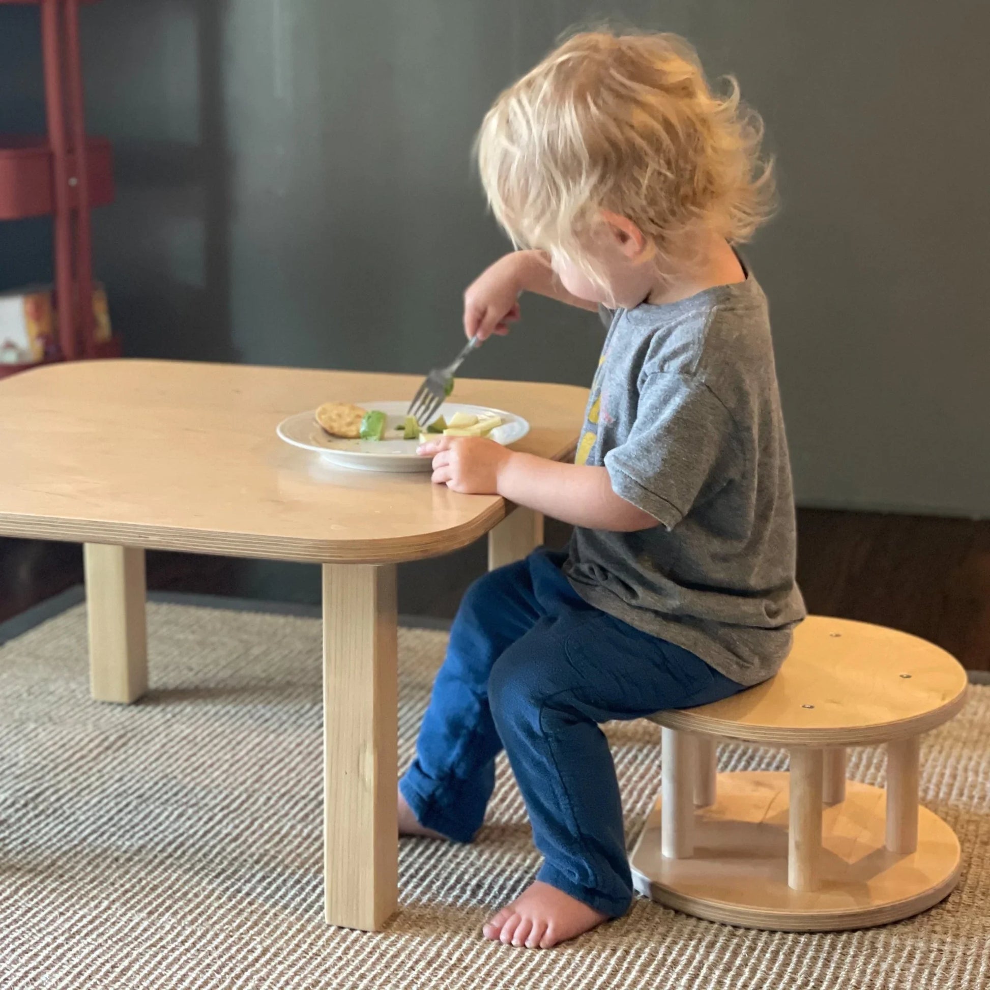 Young child eating at a sensory-friendly wooden table and chair set, barefoot on rug