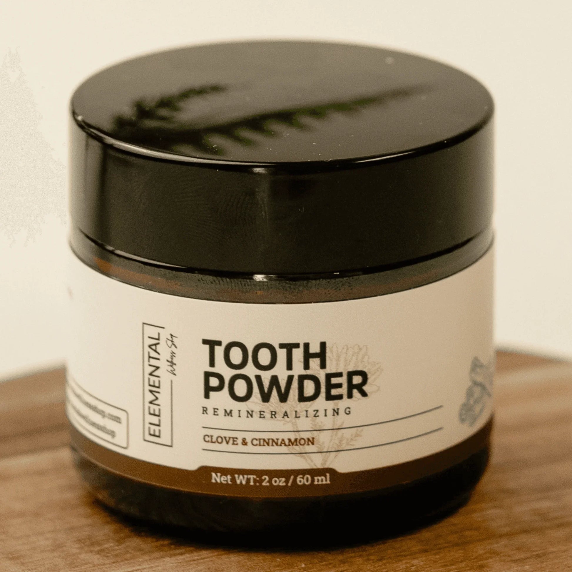 Clove and cinnamon remineralizing tooth powder in amber jar on wooden surface