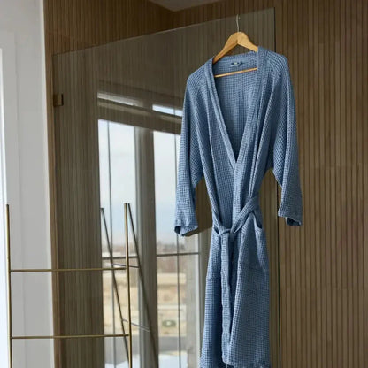 Blue sensory-friendly waffle robe with belt hanging on wooden hanger in modern bathroom