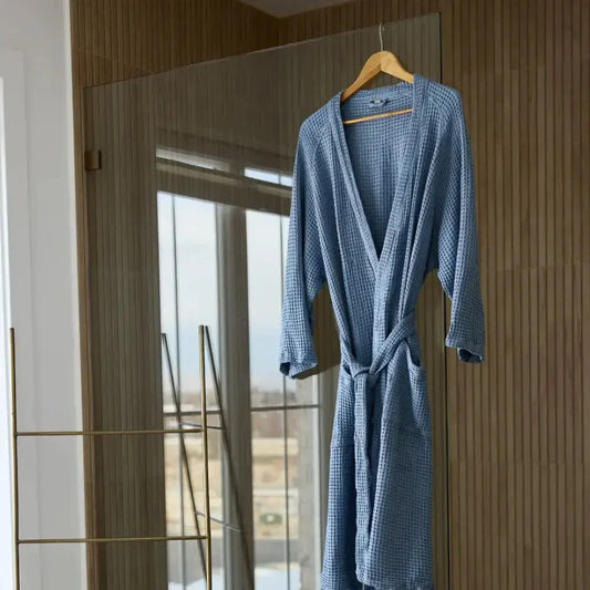 Blue sensory-friendly waffle robe with belt hanging on wooden hanger in modern bathroom