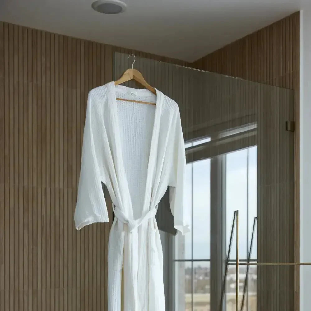 White sensory-friendly robe with belt hanging in modern bathroom with wood and glass accents