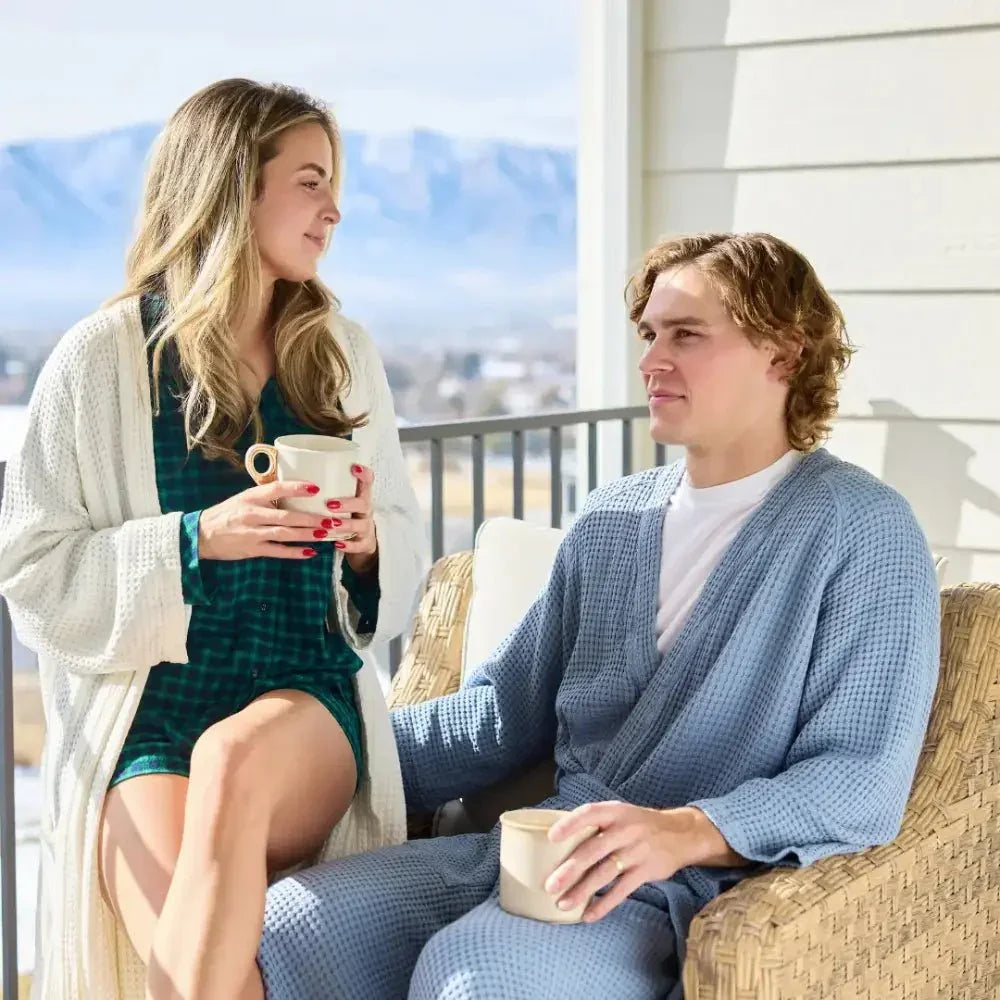 Two people in cozy robes enjoying coffee on a sunny porch with mountain views