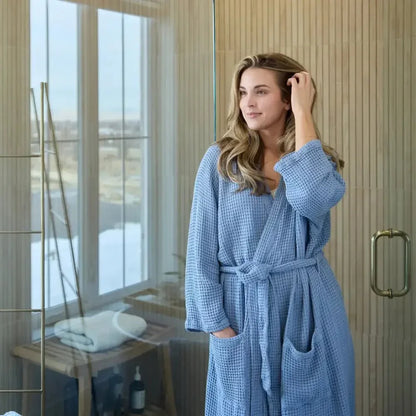 Woman in light blue waffle robe standing in a modern bathroom with wooden accents