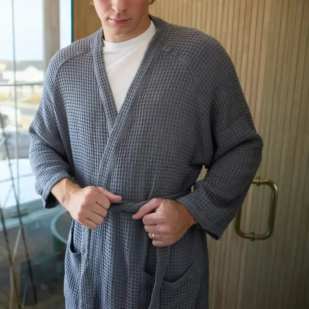 Man wearing a waffle-knit gray sensory-friendly robe, tying waist belt indoors
