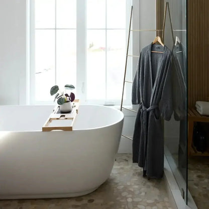 Gray textured bathrobe hanging in modern bathroom with white bathtub and natural light