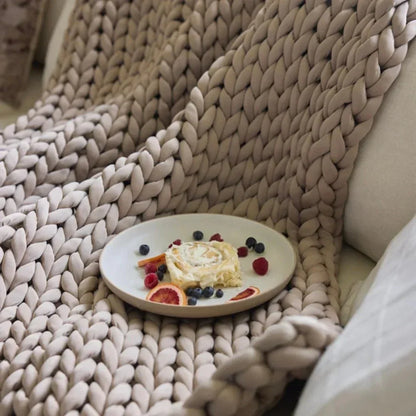 Chunky knit weighted blanket in beige on a sofa with a plate of pastry and fresh berries