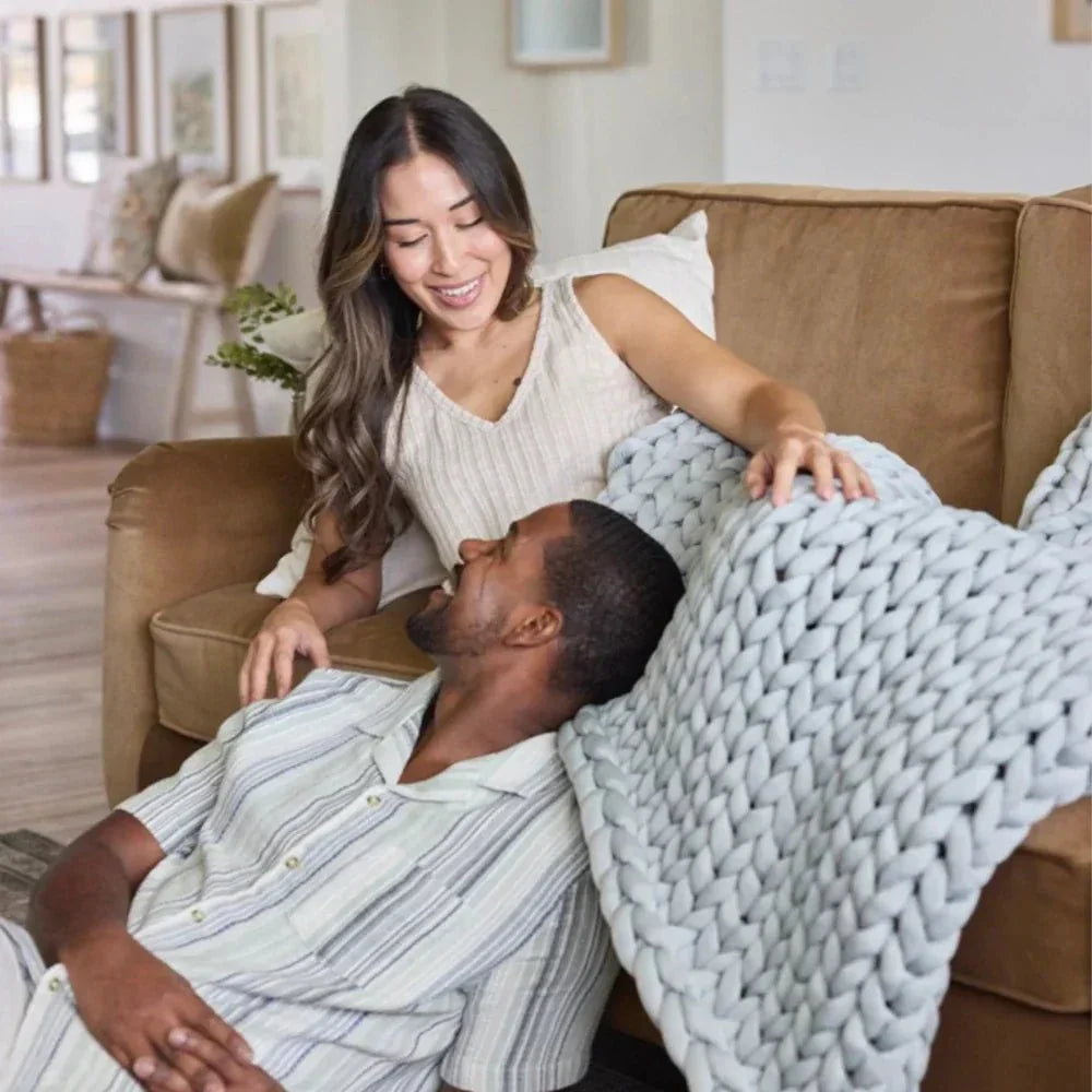 Couple relaxing with chunky knit cooling weighted blanket on brown couch in cozy living room