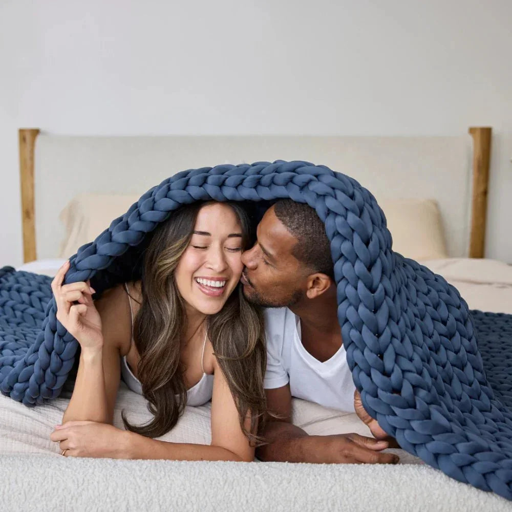 Happy couple cuddling under chunky knit blue weighted blanket on bed