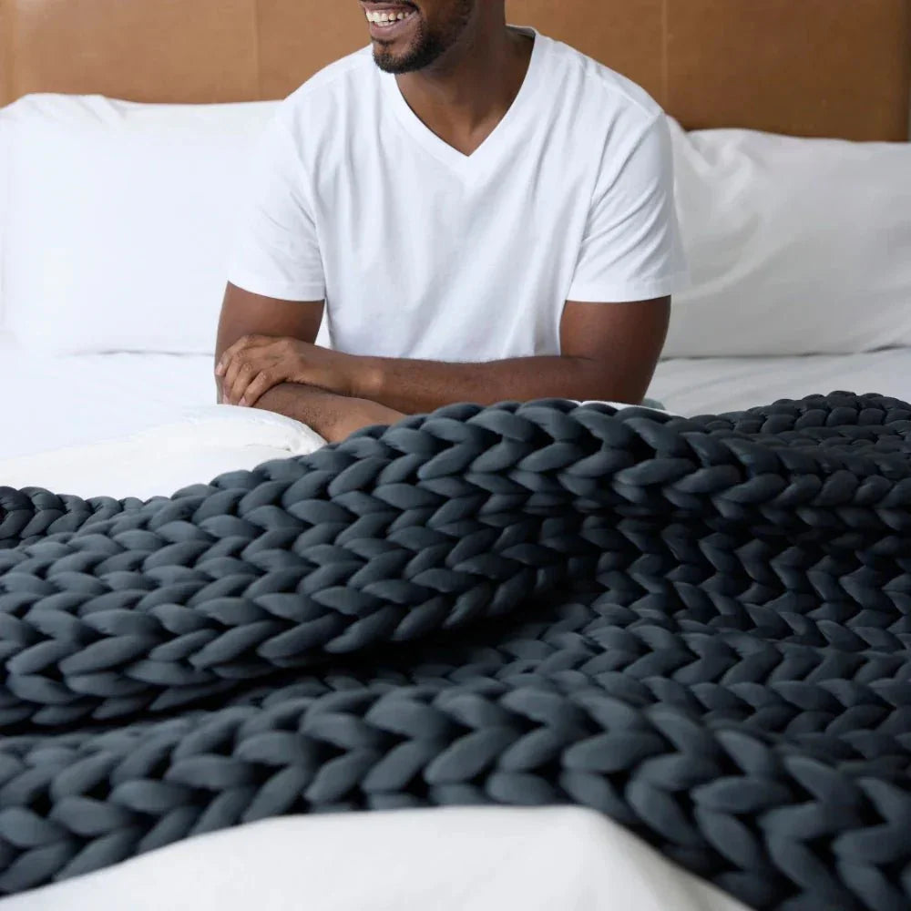 Man sitting on bed with chunky knit dark grey weighted blanket, sensory-friendly bedding