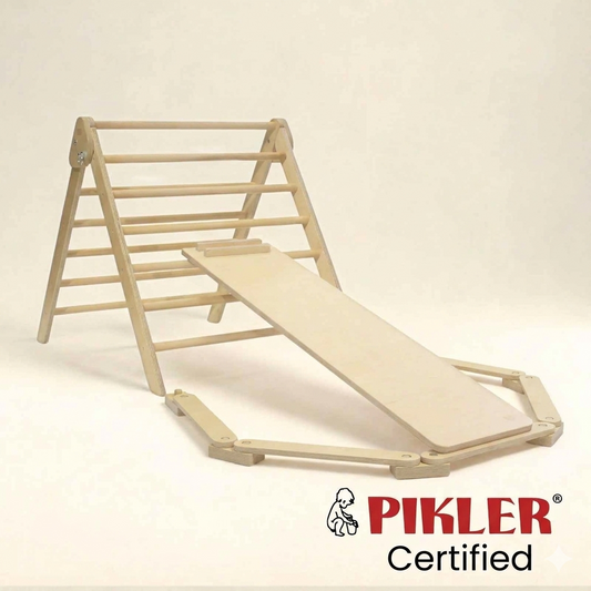 A light natural wood baby climbing and sliding play structure on a plain light beige background, with the PIKLER Certified logo at the bottom right.