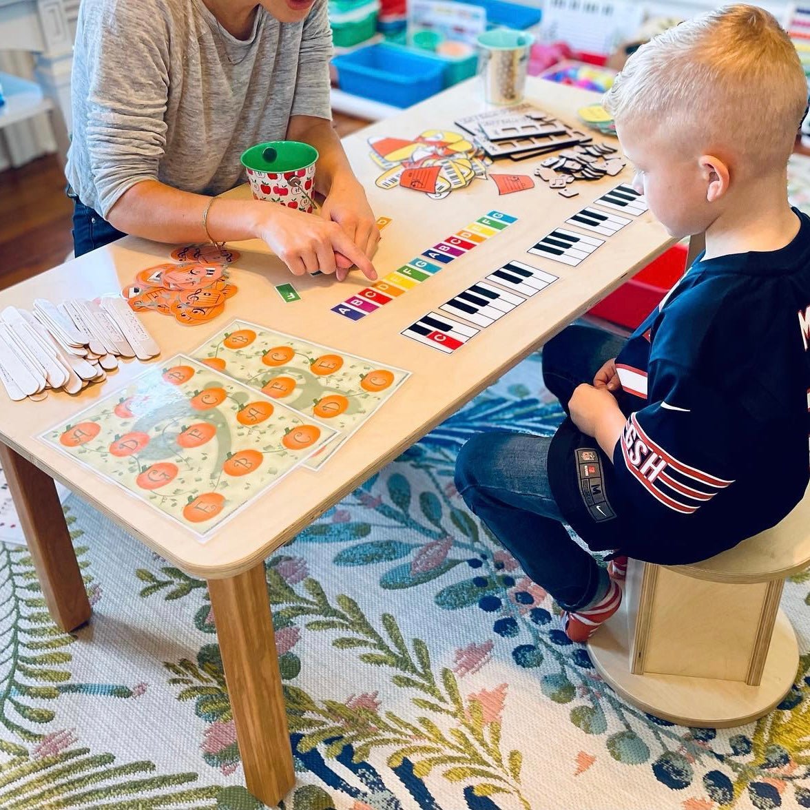 Two children playing with a toy piano and educational materials on a colorful rug.
