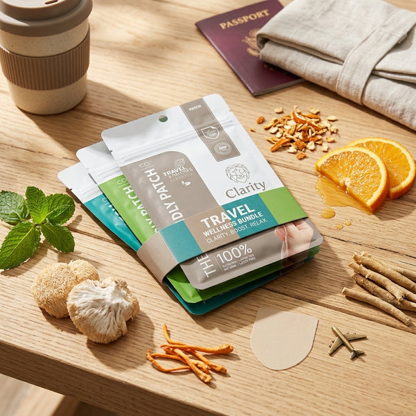 A stack of patches in resealable pouches sits on a wooden table surrounded by styled ingredients including sliced oranges, mushrooms, mint, and a passport, suggesting a travel-themed product presentation.