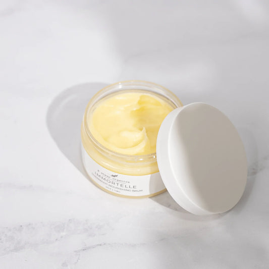 Open glass jar of yellow nourishing balm with white lid on marble surface