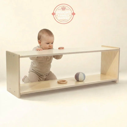 Baby kneeling by Montessori-style wooden shelf with sensory toys in neutral space