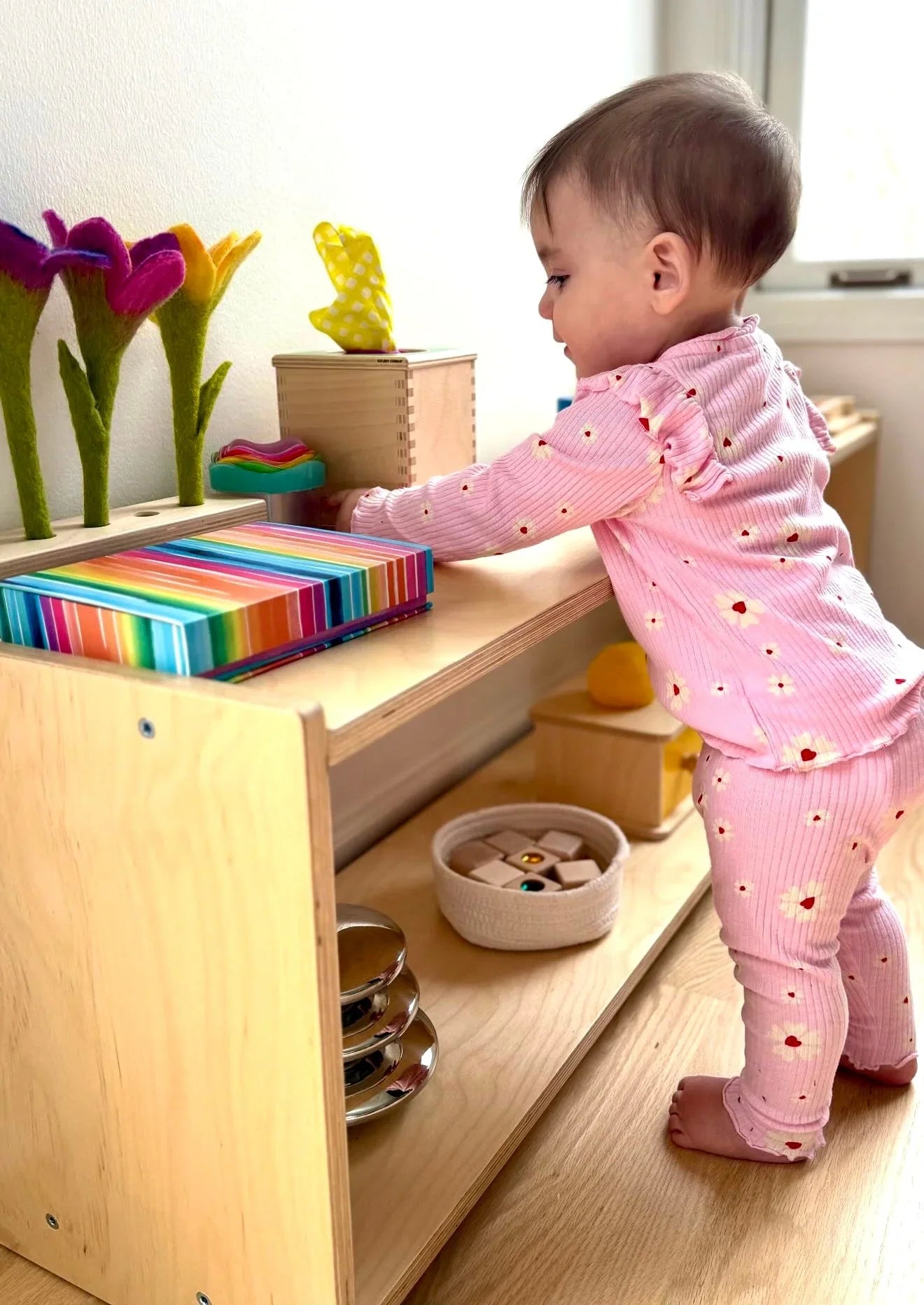 Toddler in pink pajamas playing with sensory toys and wooden blocks on a shelf