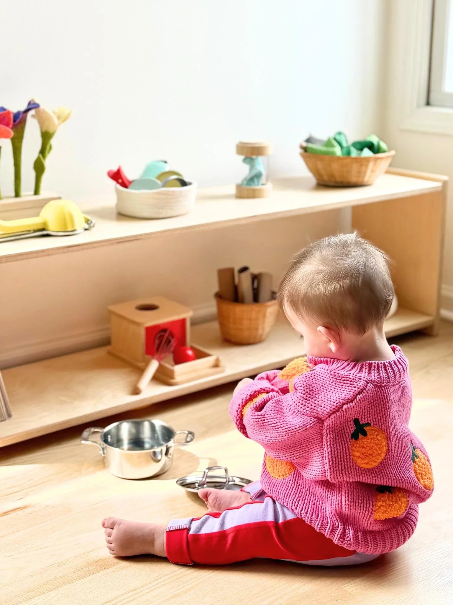 Toddler in pink sweater with orange pattern playing with sensory toys on wooden floor