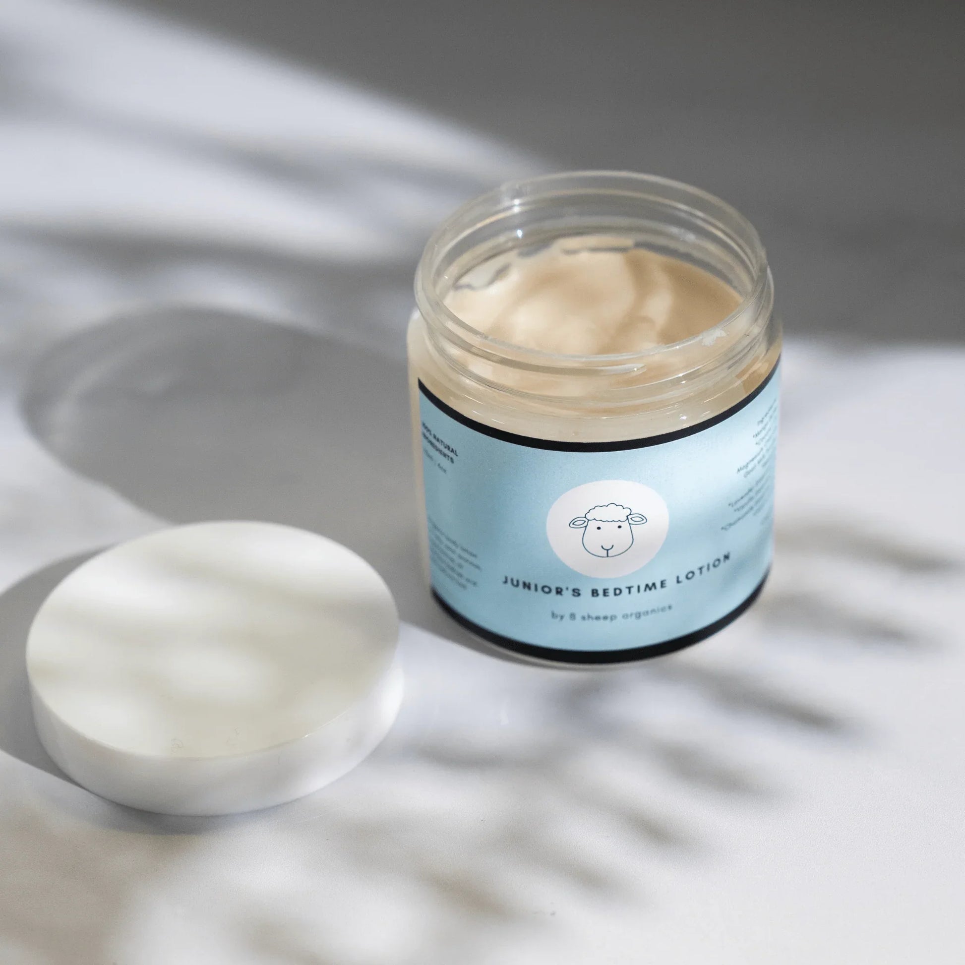 Open jar of Junior's Bedtime Lotion for kids with a light blue label on a white surface