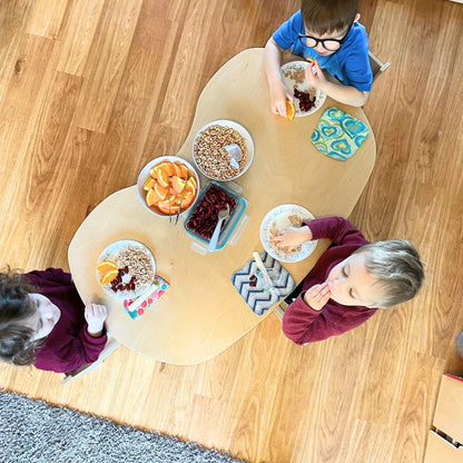 Kidney-shaped sensory-friendly snack table with three kids eating cereal, oranges, and cherries.