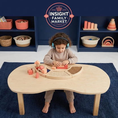 Child wearing headphones plays with sensory blocks at a wooden table in a calm playroom.