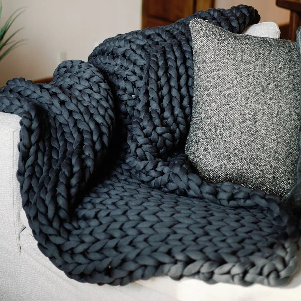 Chunky charcoal weighted blanket draped over a sofa next to a textured pillow