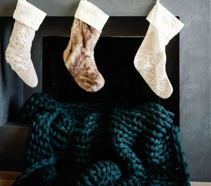 Chunky forest green knit sensory blanket draped on fireplace with stockings above