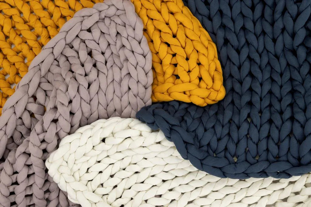 Chunky knit blankets in marigold, blue, rose, and cream, layered for a cozy, sensory-friendly look.