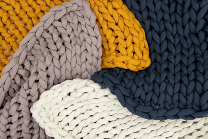 Chunky knit blankets in marigold, blue, rose, and cream, layered for a cozy, sensory-friendly look.