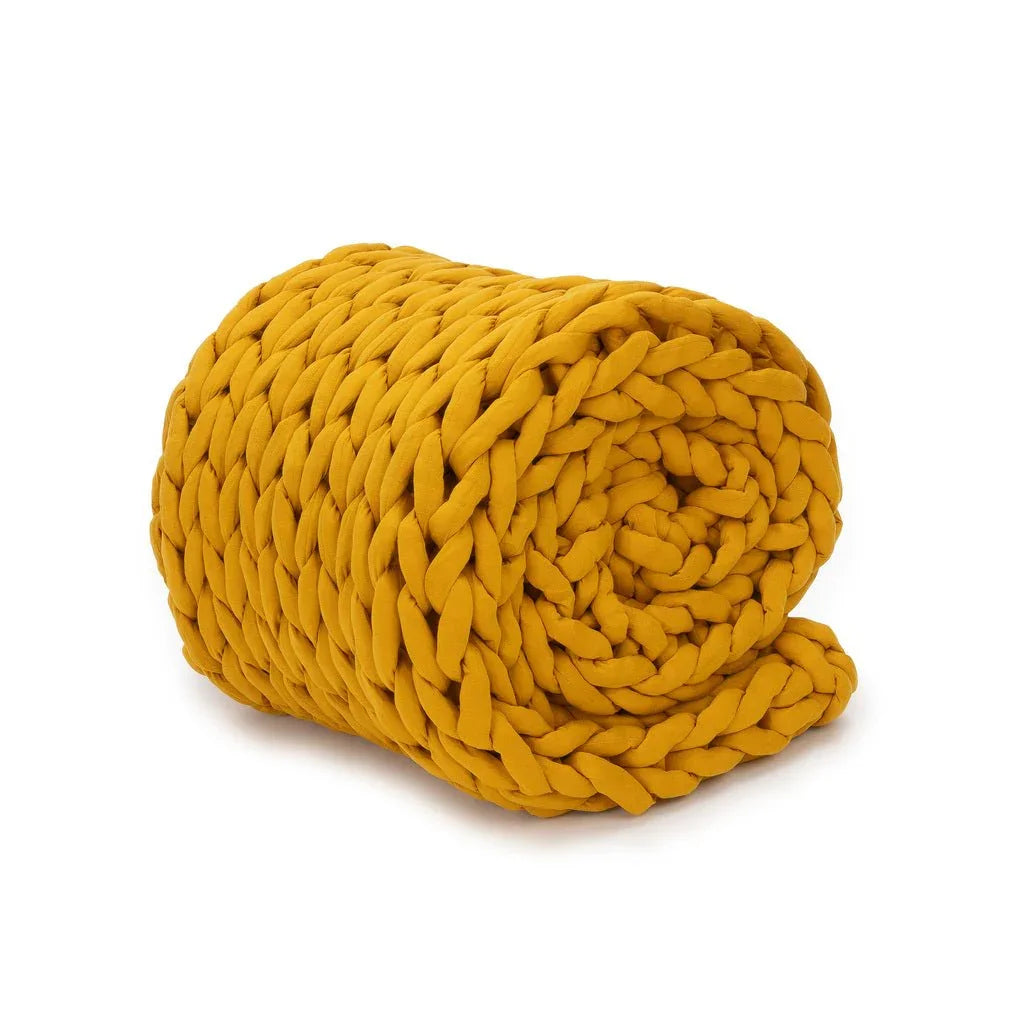 Chunky knit marigold weighted blanket rolled up on white background, sensory-friendly bedding.