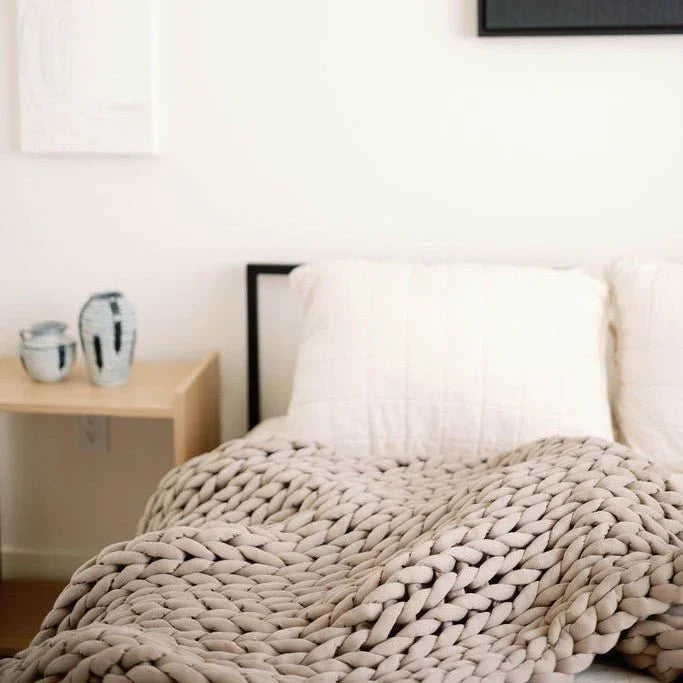 Chunky knit taupe weighted blanket on bed with white pillows, minimal bedroom decor