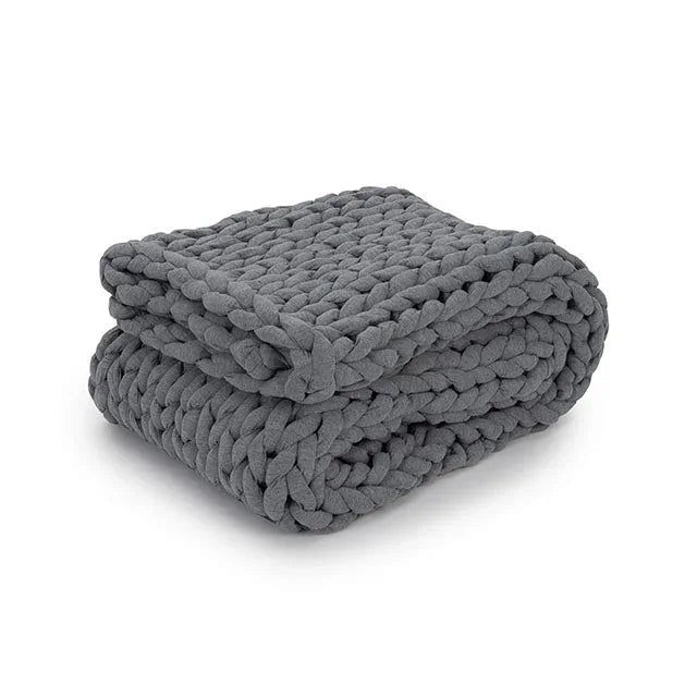 Folded chunky knit gray weighted blanket, sensory-friendly home comfort item on white background.