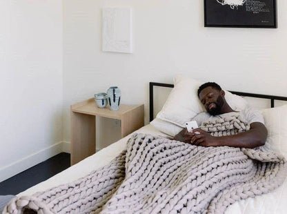 Man relaxing on bed with chunky knit weighted blanket in modern bedroom