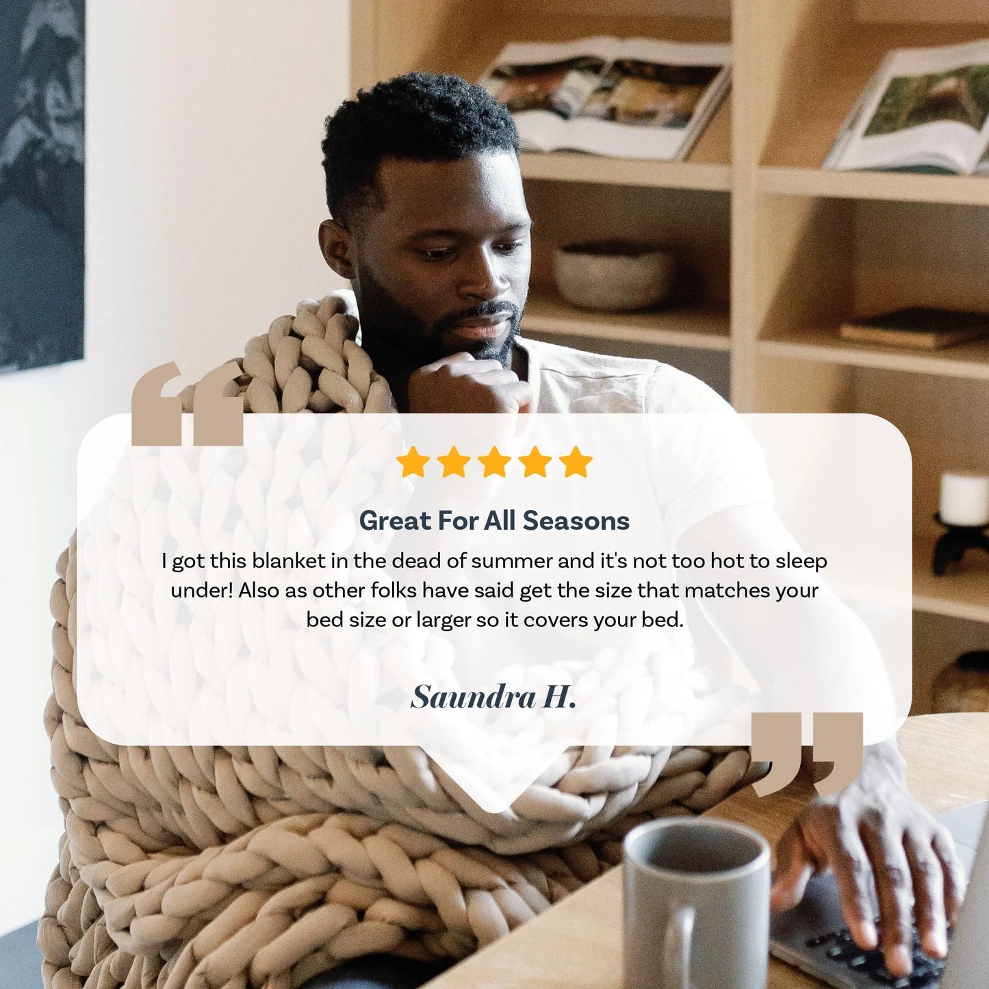 Man using laptop while wrapped in chunky taupe weighted blanket, reading customer review.