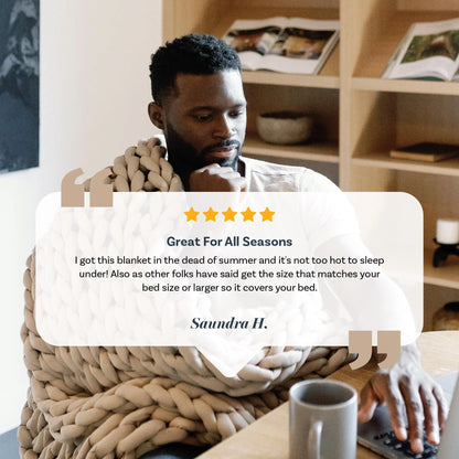Man using laptop while wrapped in chunky taupe weighted blanket, reading customer review.