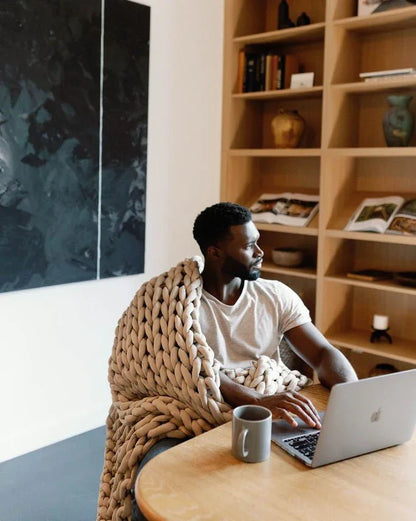 Man using laptop with taupe chunky knit weighted blanket, cozy home office, sensory-friendly decor.