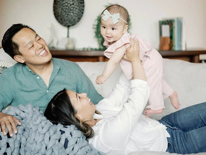 Smiling parents on couch holding up baby girl in soft pink sensory-friendly outfit