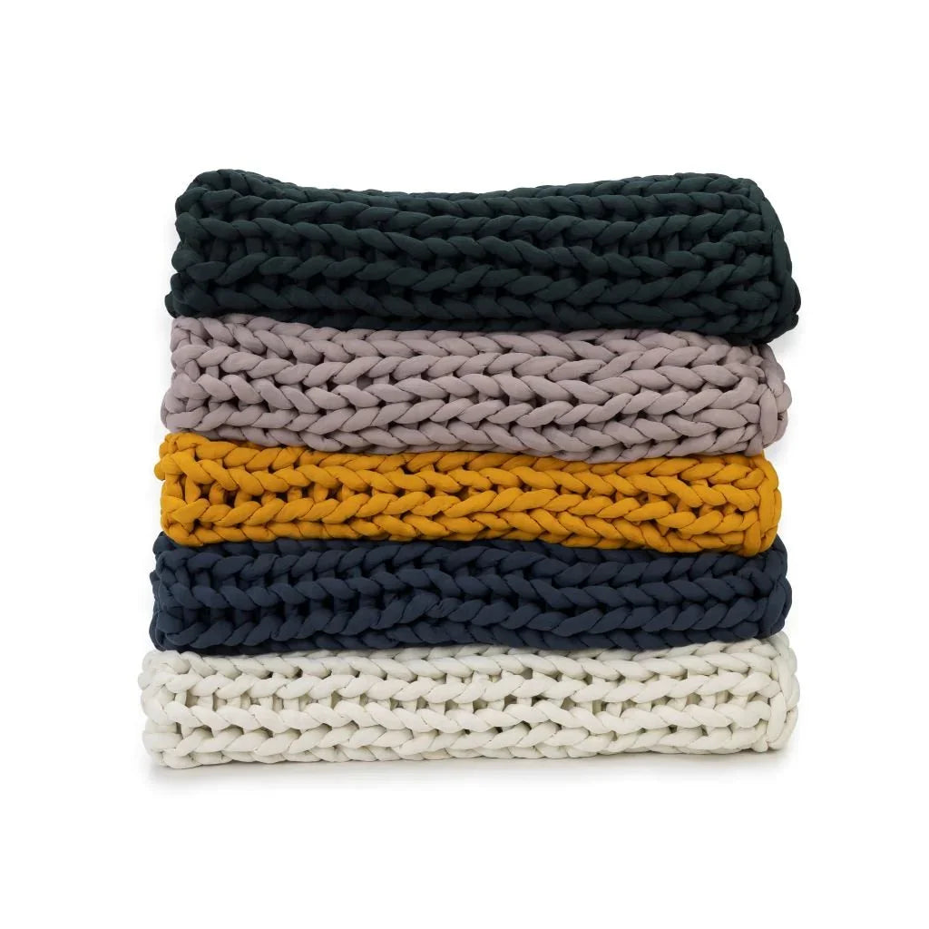 Stack of chunky knit sensory-friendly blankets in forest green, rose, marigold, blue, and cream