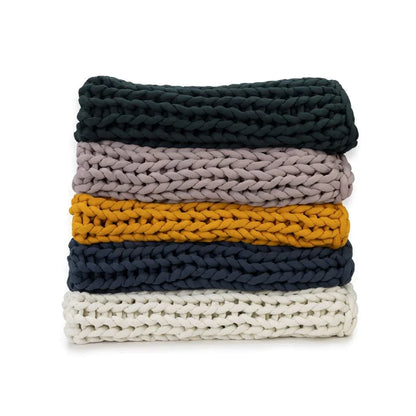 Stack of chunky knit sensory-friendly blankets in forest green, rose, marigold, blue, and cream