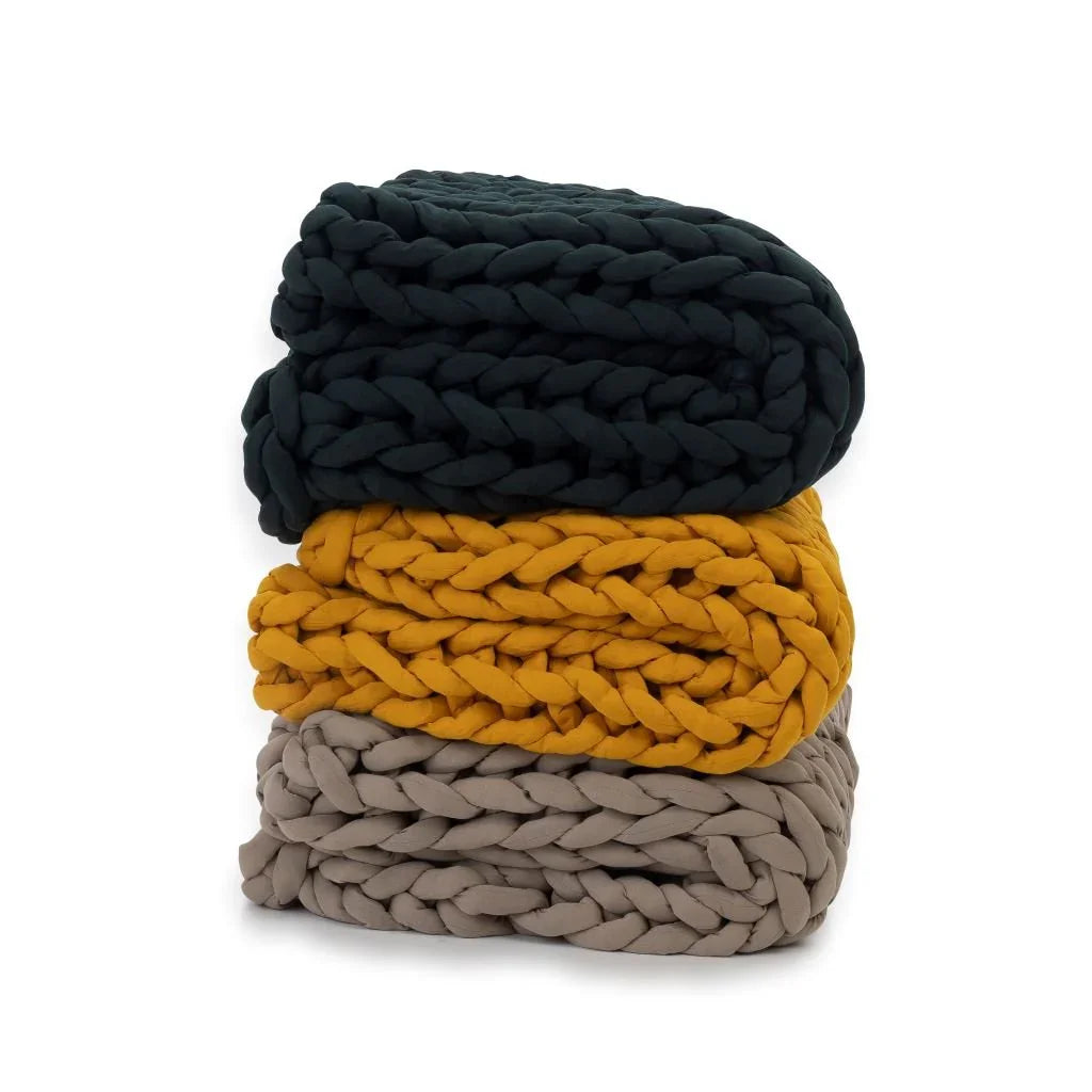 Stack of chunky knit sensory blankets in dark green, mustard yellow, and taupe on white background