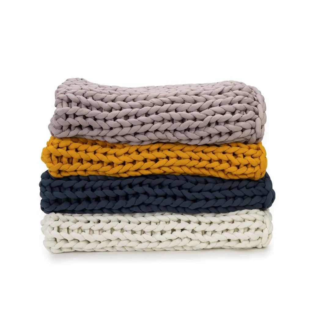 Stack of four chunky knit blankets in rose, marigold, blue, and cream colors