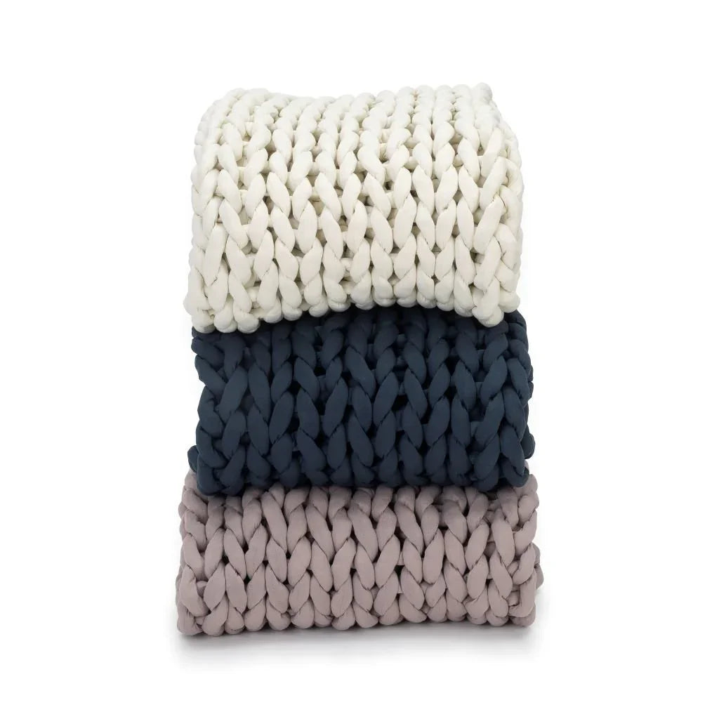 Stack of three chunky knit sensory-friendly weighted blankets in cream, navy, and taupe