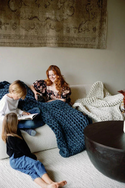 Woman and children relaxing on sofa with chunky knit sensory blankets in cozy living room