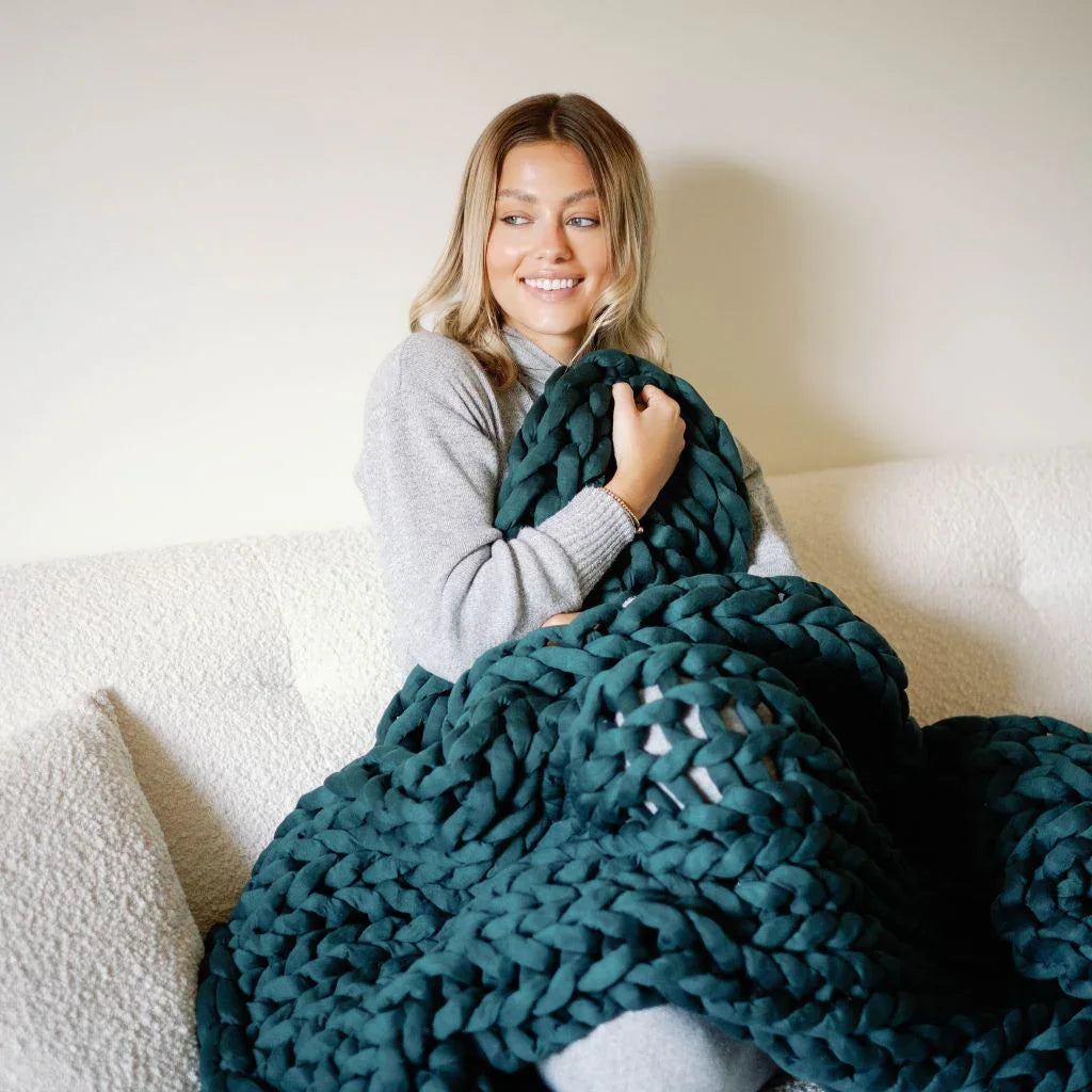 Woman on sofa wrapped in chunky forest green weighted blanket, sensory-friendly home comfort