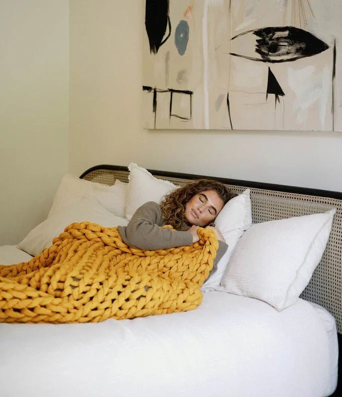 Woman sleeping under a chunky yellow sensory blanket on a bed with white pillows.